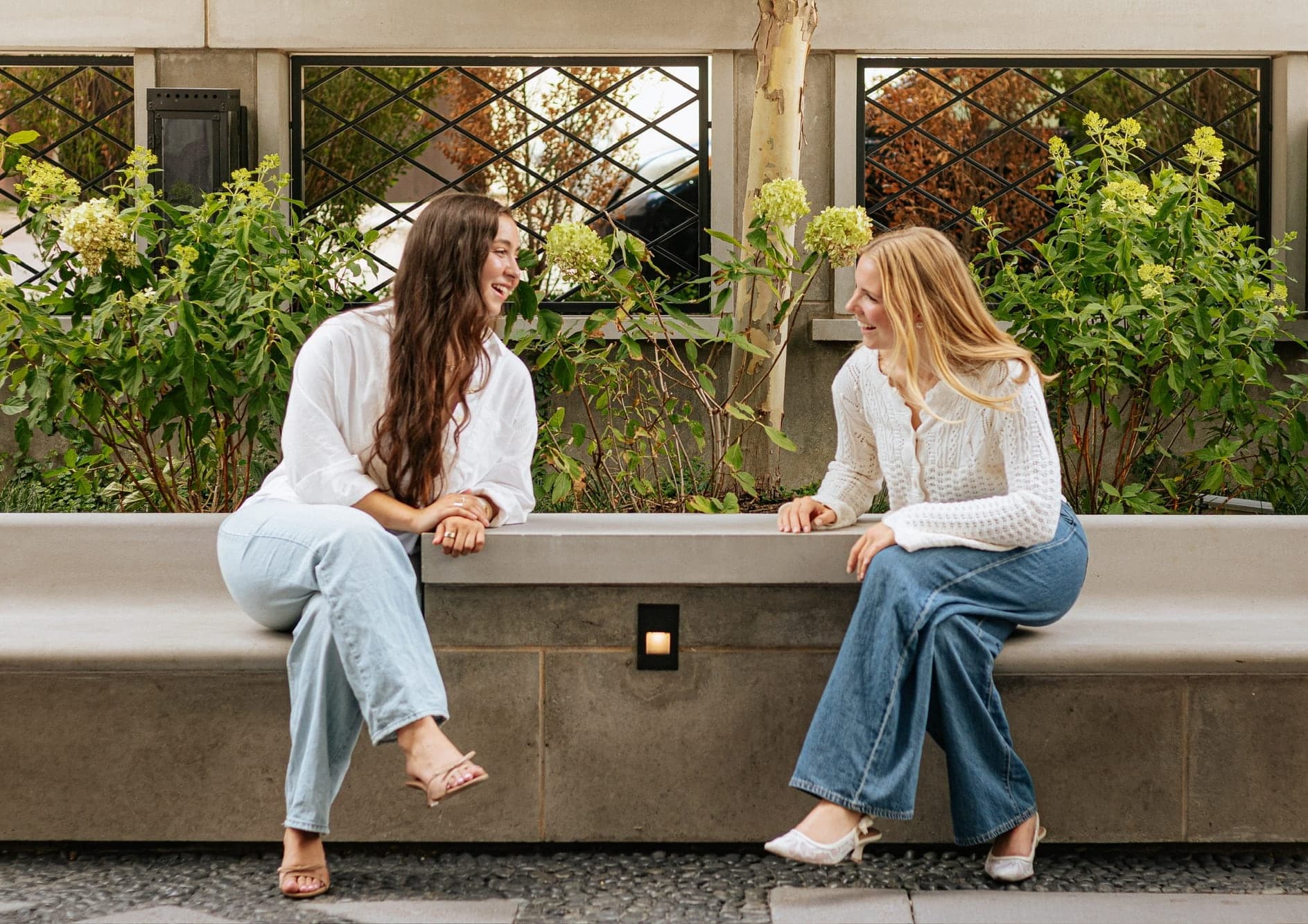 Lindsay (left) and Maddie (right), the founders of Petal Punch, sitting on a garden bench and laughing together